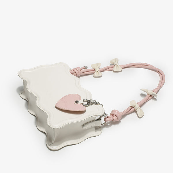 Small structured scalloped-edge shoulder bag with bow-tied pink cord strap and silver heart charm pendant, detail view 3