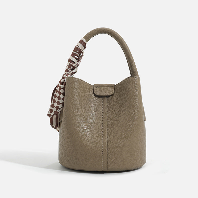 Pebbled leather-look bucket bag with checkered scarf-wrapped top handle, flap tab closure, gold-tone hardware, and matching