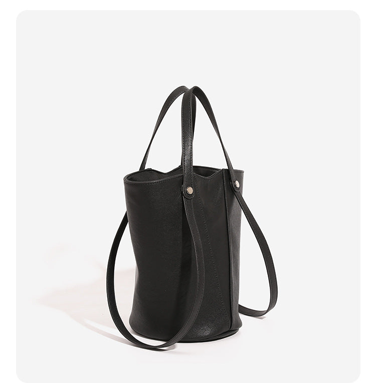 Structured black leather-look bucket tote bag with slim shoulder straps, silver-tone stud hardware, and tapered body, detail