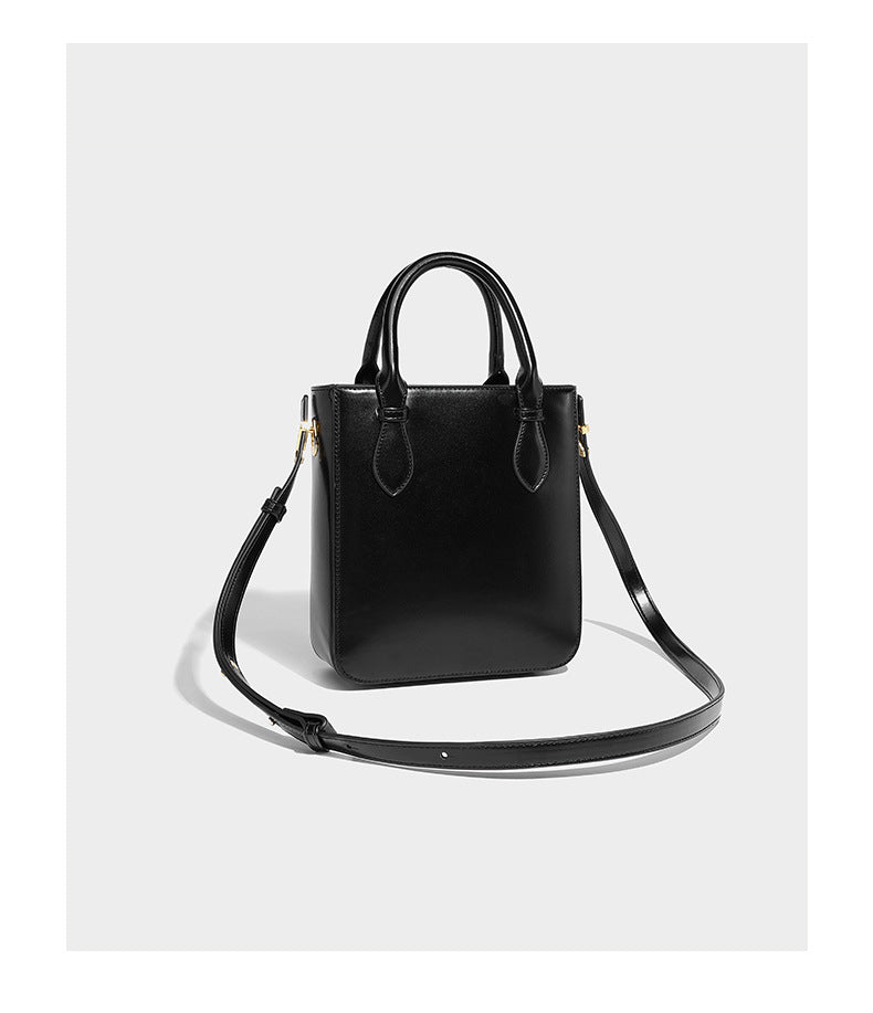 Kleine, strukturierte, kastenförmige Henkeltasche mit goldfarbenem, handförmigem Metallbeschlag in schwarzer Lederoptik mit abnehmbarem Detail