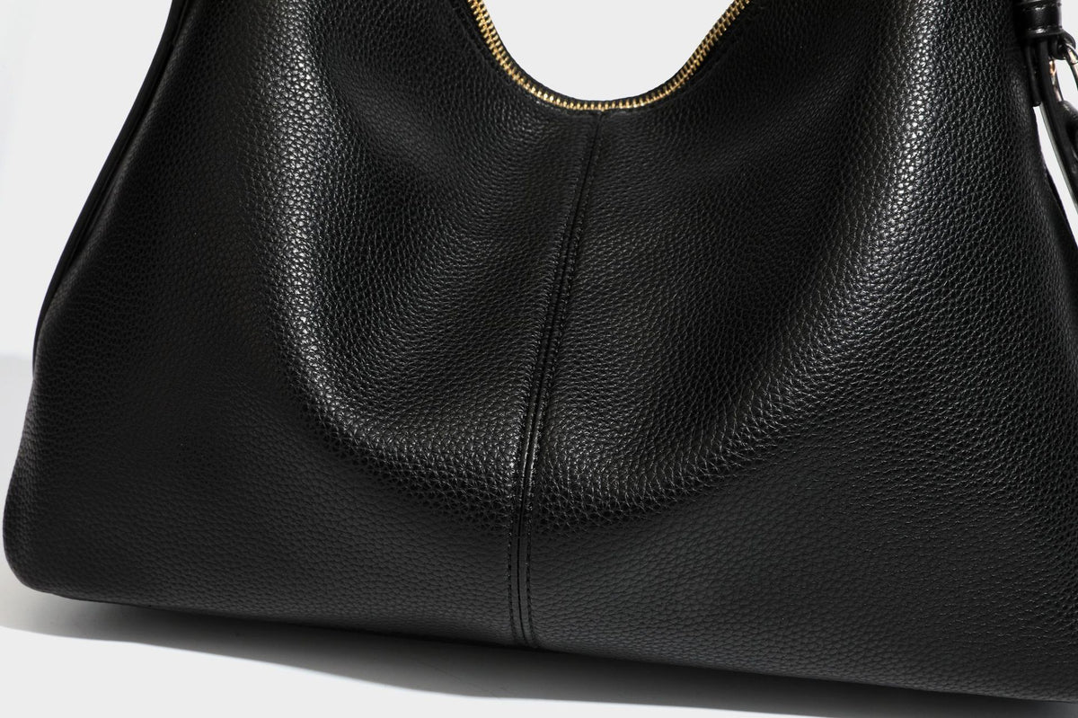 Slouchy hobo shoulder bag with pebbled leather-look finish, zip-top closure, gold-tone hardware, and hanging bead charm
