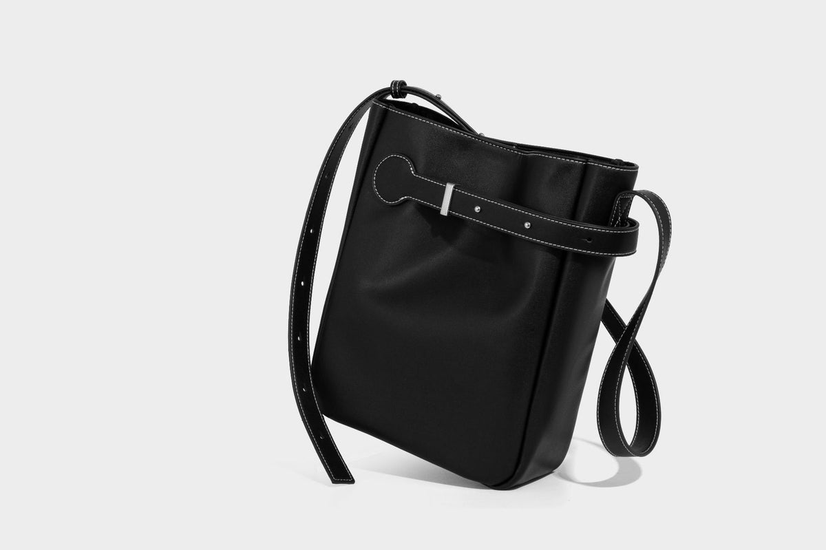 Structured dark brown leather-look bucket bag with white contrast stitching, front wraparound belt buckle strap, and long