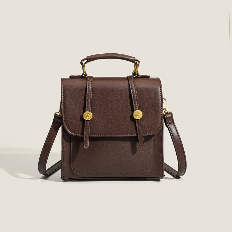 Structured mini satchel backpack with smooth leather-look finish, front flap pocket, gold-tone stud closures, and top handle