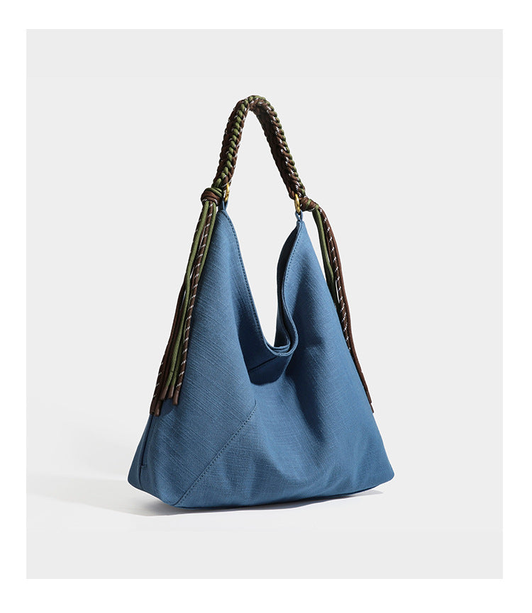 Soft slouchy cream canvas shoulder tote with braided brown and green cord handle, gold-tone ring hardware, and tassel trim