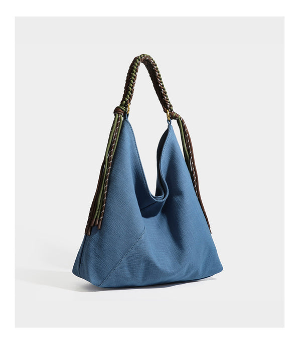 Soft slouchy cream canvas shoulder tote with braided brown and green cord handle, gold-tone ring hardware, and tassel trim
