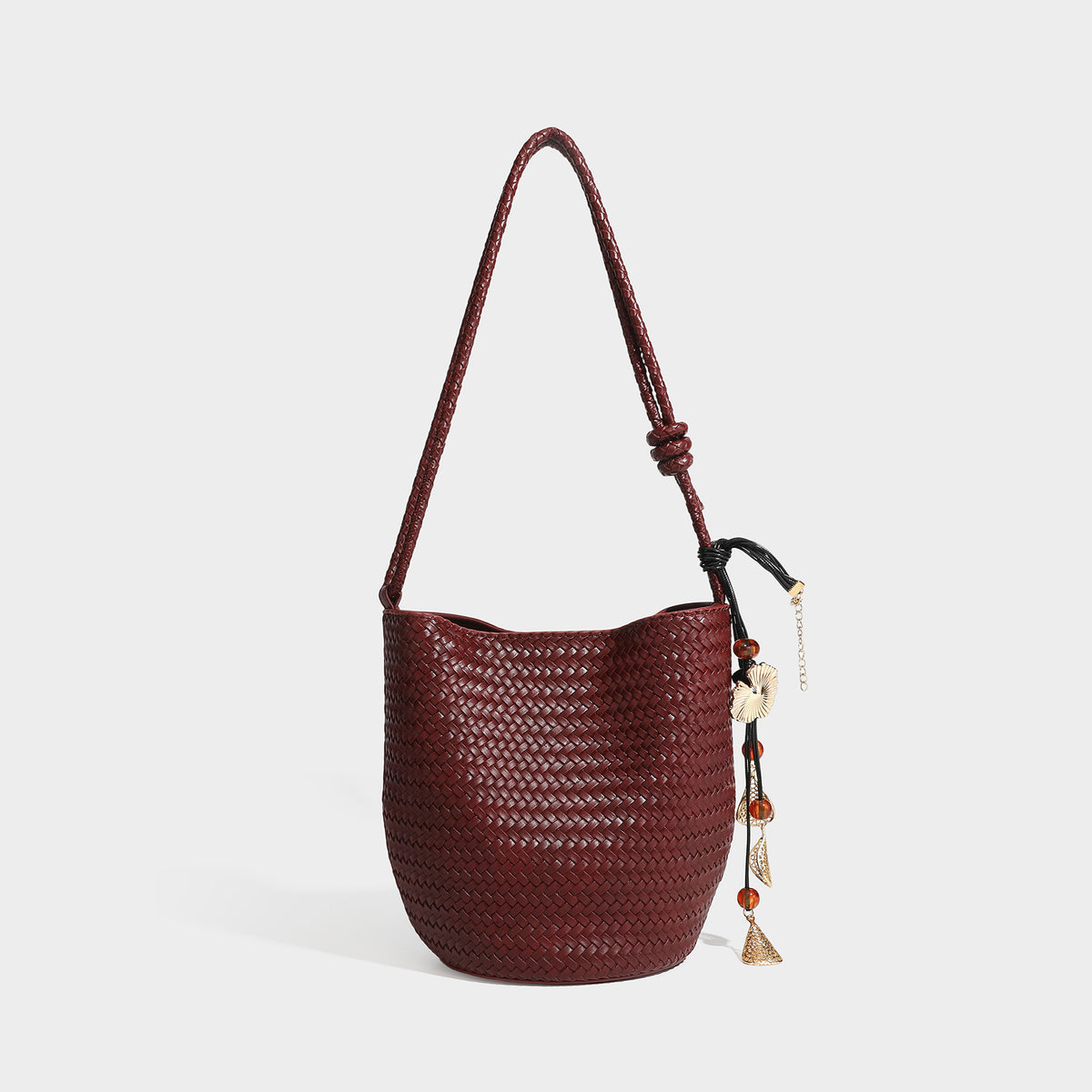 Olive green woven leather-look bucket bag with braided crossbody strap, knotted adjustment, and gold-tone tassel charm with