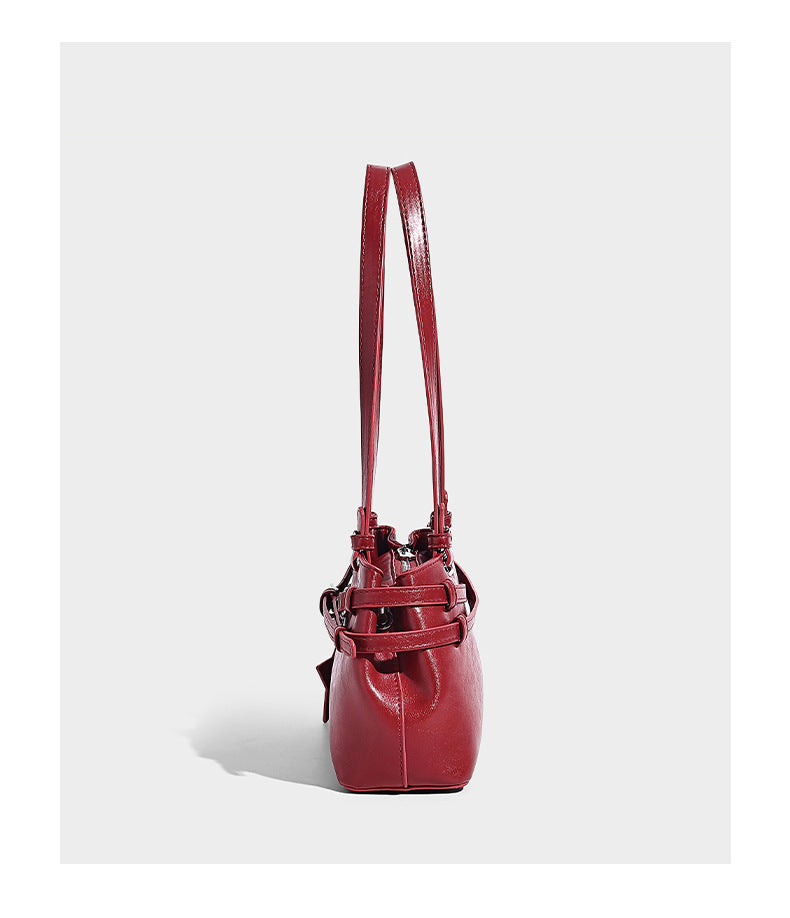 Structured glossy leather-look shoulder bag with wraparound belt straps, silver-tone hardware, and dangling star charm