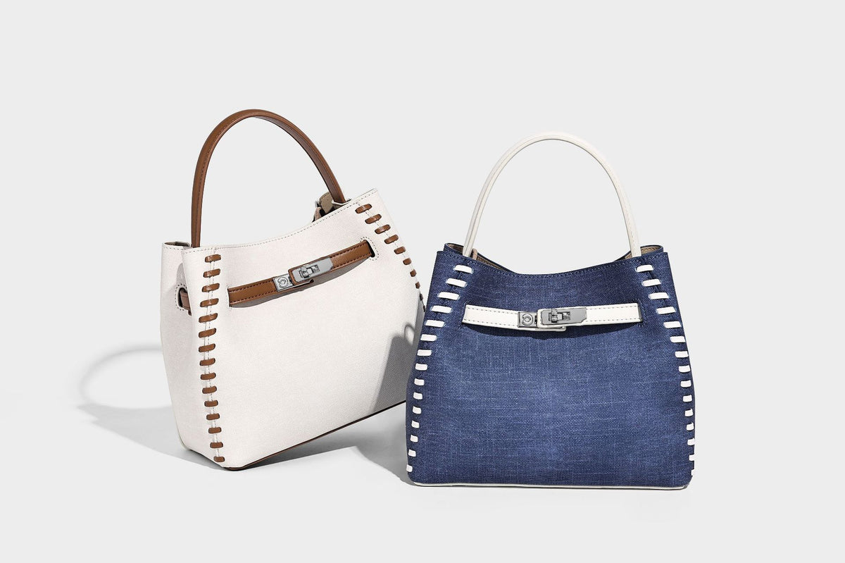 Formstabile Beuteltasche aus Denim mit weißem Zierstich-Besatz, silberfarbenem Drehverschluss, kurzen Henkeln und einem langen verstellbaren