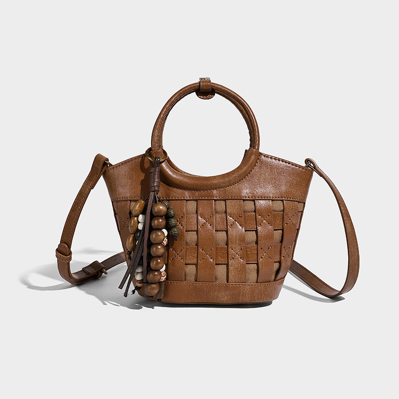 Small woven-panel bucket bag with circular ring handles, beaded tassel charm, and detachable crossbody strap in brown, detail