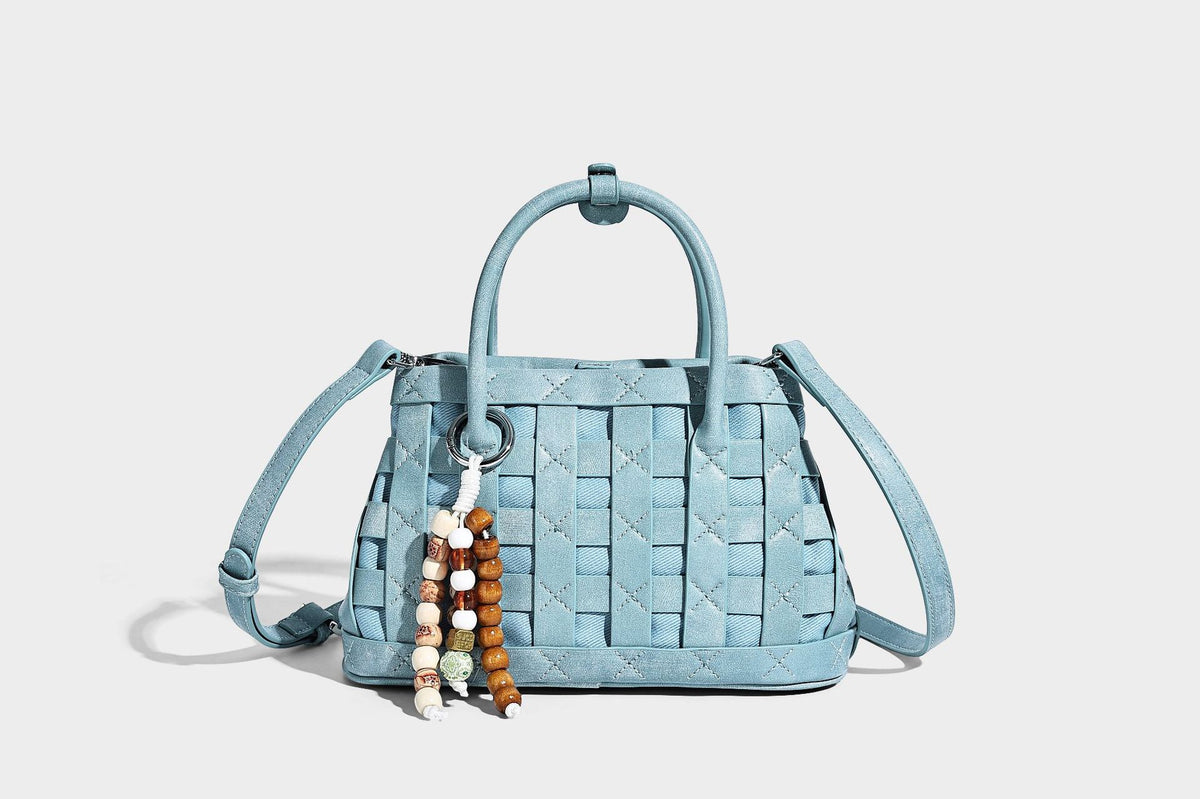 Small structured woven satchel tote with rounded top handles, silver-tone ring hardware, and bead tassel charm, detail view