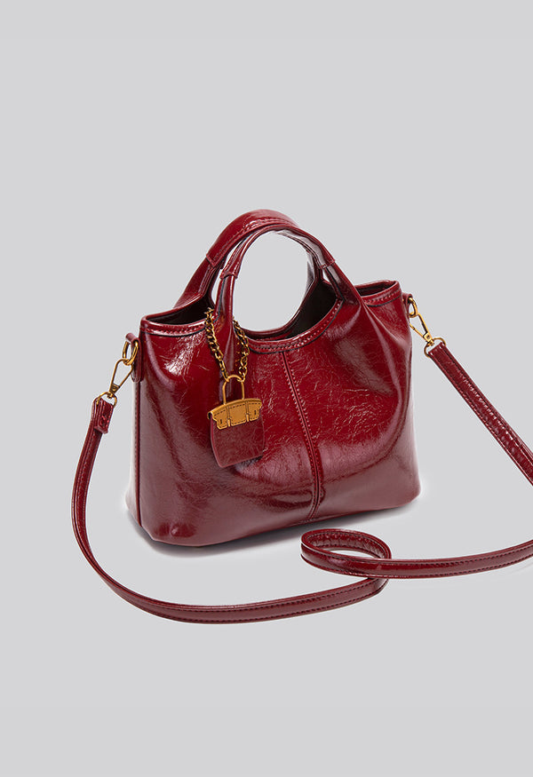 Structured crinkle-gloss top-handle satchel in deep burgundy with antique gold lock charm and detachable shoulder strap