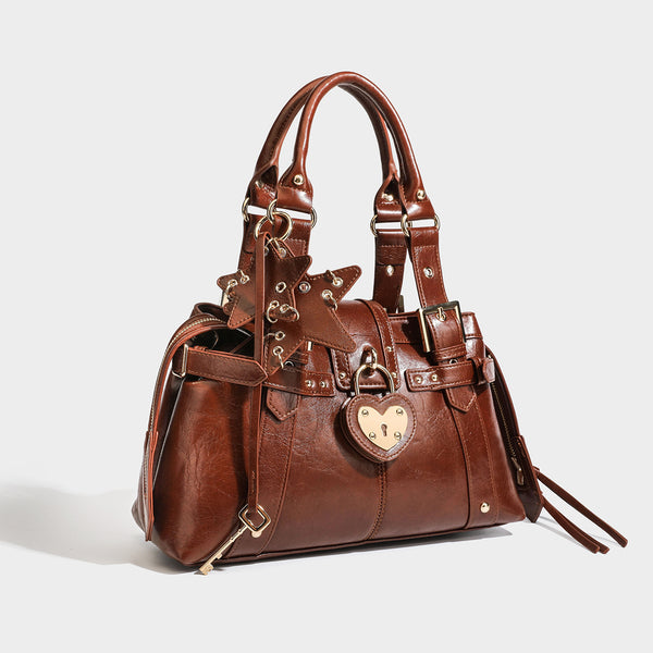 Structured leather-look satchel bag with heart padlock charm, star charm, gold-tone buckle hardware, dual top handles, and