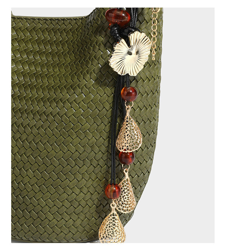 Olive green woven leather-look bucket bag with braided crossbody strap, knotted adjustment, and gold-tone tassel charm with