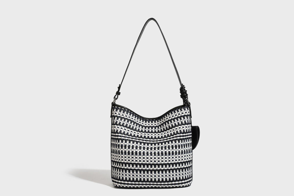 Woven stripe bucket shoulder bag in cream and dark brown with leather-look trim, knotted adjustable strap, and small shield
