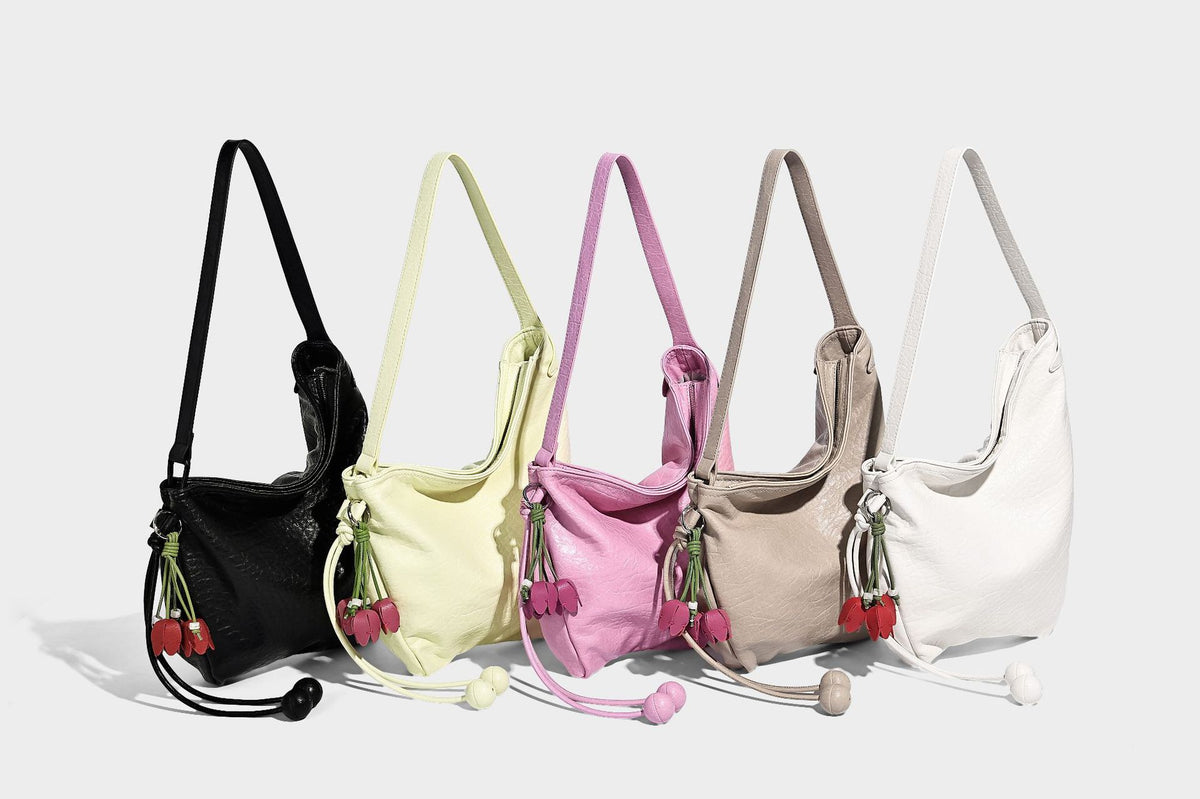 Slouchy hobo shoulder bag in pale yellow with slim strap, drawstring bead closure, and pink tulip floral charm, detail view