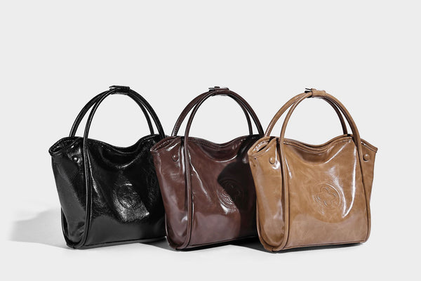 Glossy leather-look structured tote bag with rounded top handles, detachable shoulder strap, embossed front emblem, and side