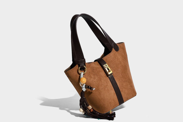 Small structured trapezoid tote bag in matte suede-look finish with black contrast trim, gold-tone front clasp, tassel charm
