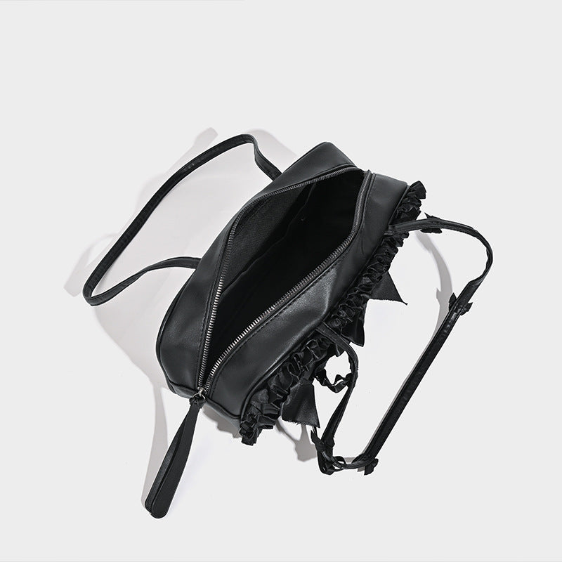 Black leather-look structured tote bag with gathered ruffle trim, ribbon bow accents, top zip closure, and attached card