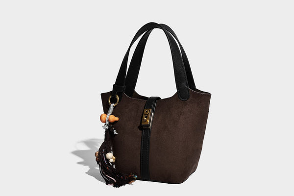 Small structured trapezoid tote bag in matte suede-look finish with black contrast trim, gold-tone front clasp, tassel charm