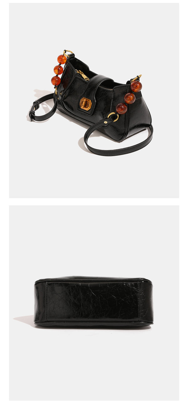 Compact glossy crinkled baguette shoulder bag with amber resin bead strap accent and gold-tone turn-lock closure, detail view