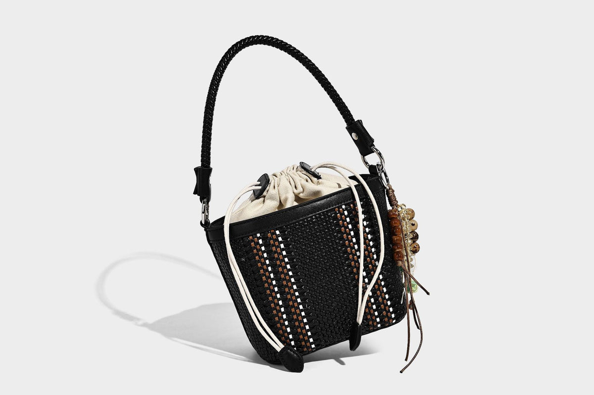 Small woven bucket bag with drawstring top, braided handle, detachable crossbody strap, and silver-tone ring hardware, detail