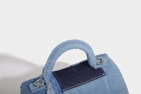 Structured patchwork denim trapezoid satchel bag with frayed panel trim, rounded top handle, and silver-tone hardware, detail