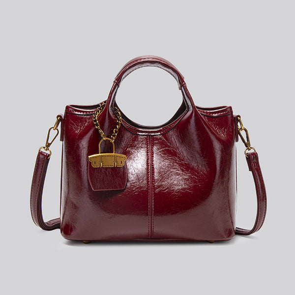 Structured crinkle-gloss top-handle satchel in deep burgundy with antique gold lock charm and detachable shoulder strap