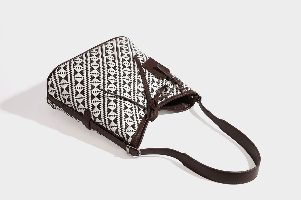 Woven geometric bucket shoulder bag in white and dark brown two-tone pattern with leather-look trim and drawstring top