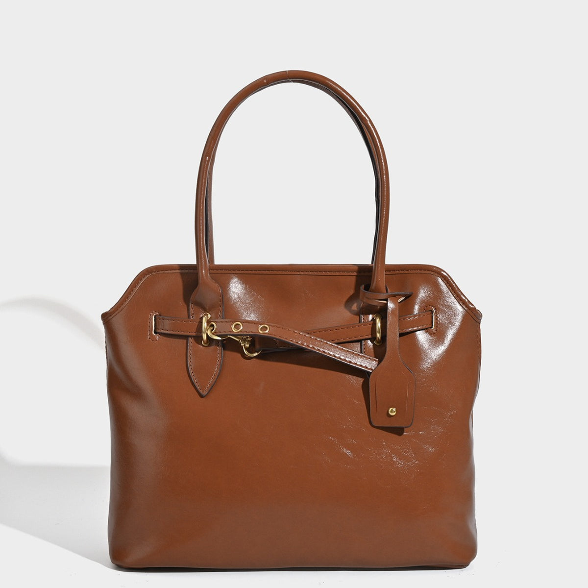 Structured cognac brown leather-look tote bag with decorative belt strap and gold-tone hardware, front view