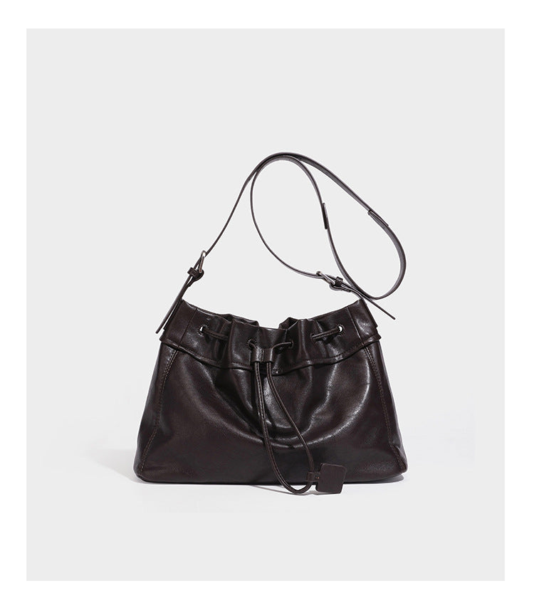 Slouchy drawstring bucket bag in dark brown leather-look finish with long adjustable shoulder strap and gathered tie closure
