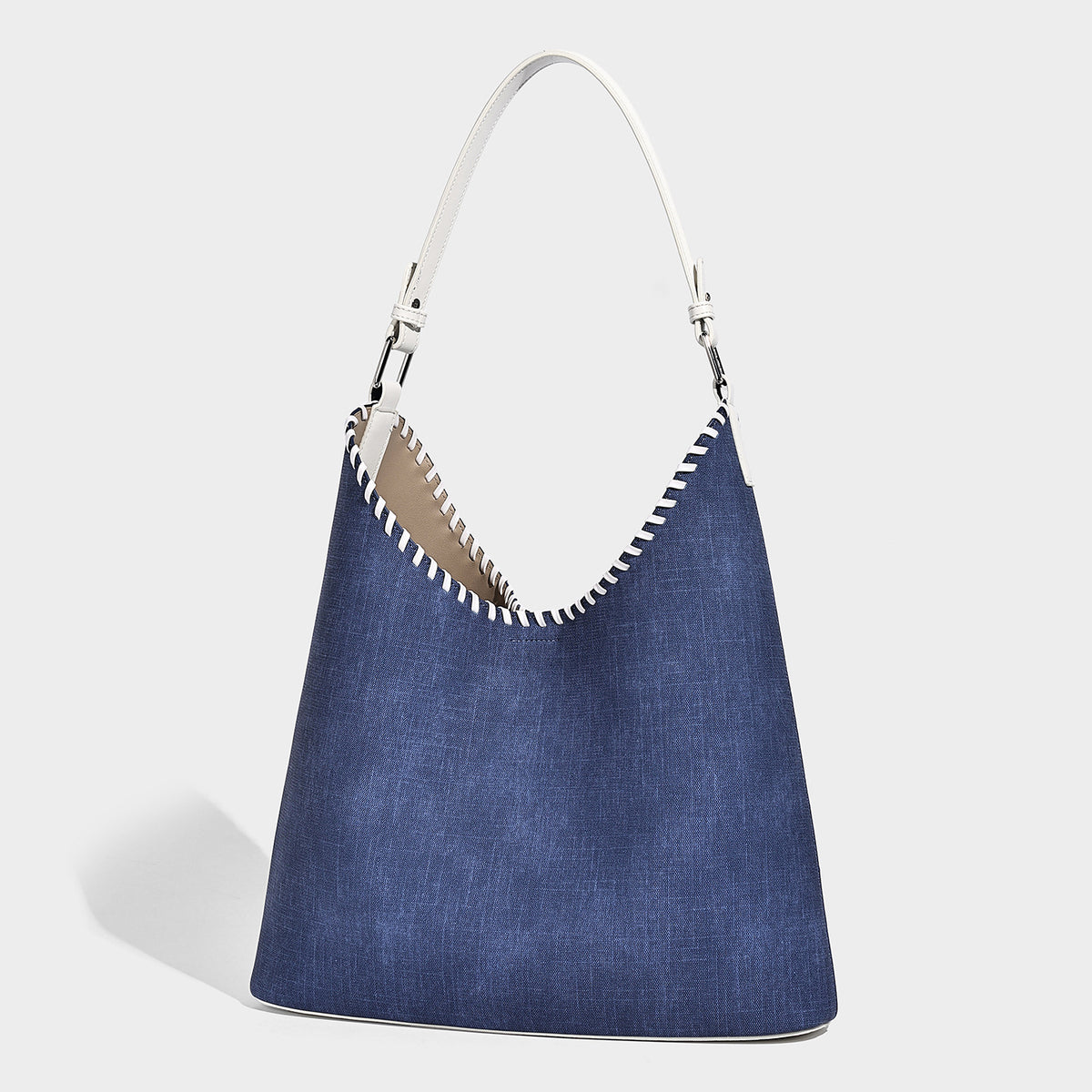 Denim-blue hobo tote with white leather-look shoulder strap, contrast whipstitch trim along curved open top, and silver-tone