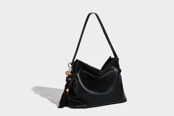 Large slouchy leather-look hobo tote bag with open top, adjustable shoulder strap, and colorful tassel bead charm, detail