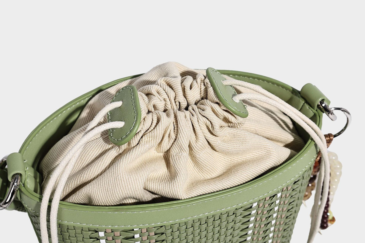 Small woven bucket bag with drawstring top, braided handle, detachable crossbody strap, and silver-tone ring hardware, detail