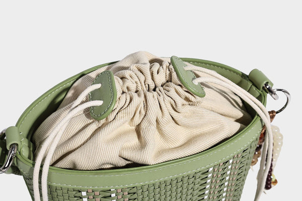 Small woven bucket bag with drawstring top, braided handle, detachable crossbody strap, and silver-tone ring hardware, detail