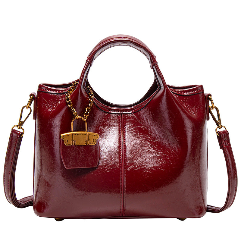 Structured crinkle-gloss top-handle satchel in deep burgundy with antique gold lock charm and detachable shoulder strap