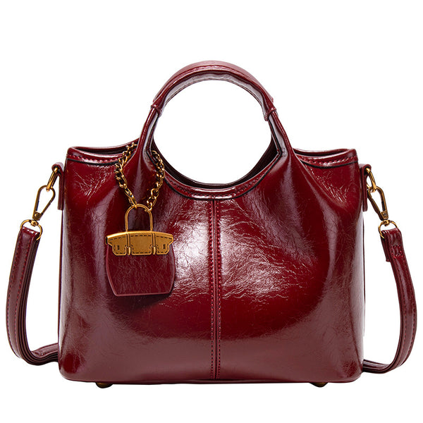 Structured crinkle-gloss top-handle satchel in deep burgundy with antique gold lock charm and detachable shoulder strap