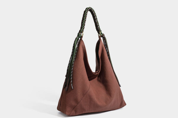 Soft slouchy cream canvas shoulder tote with braided brown and green cord handle, gold-tone ring hardware, and tassel trim