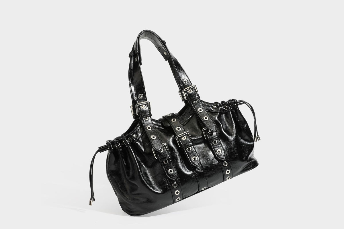 Large black glossy leather-look tote bag with silver buckle straps, eyelet grommet panels, drawstring side gathers, and