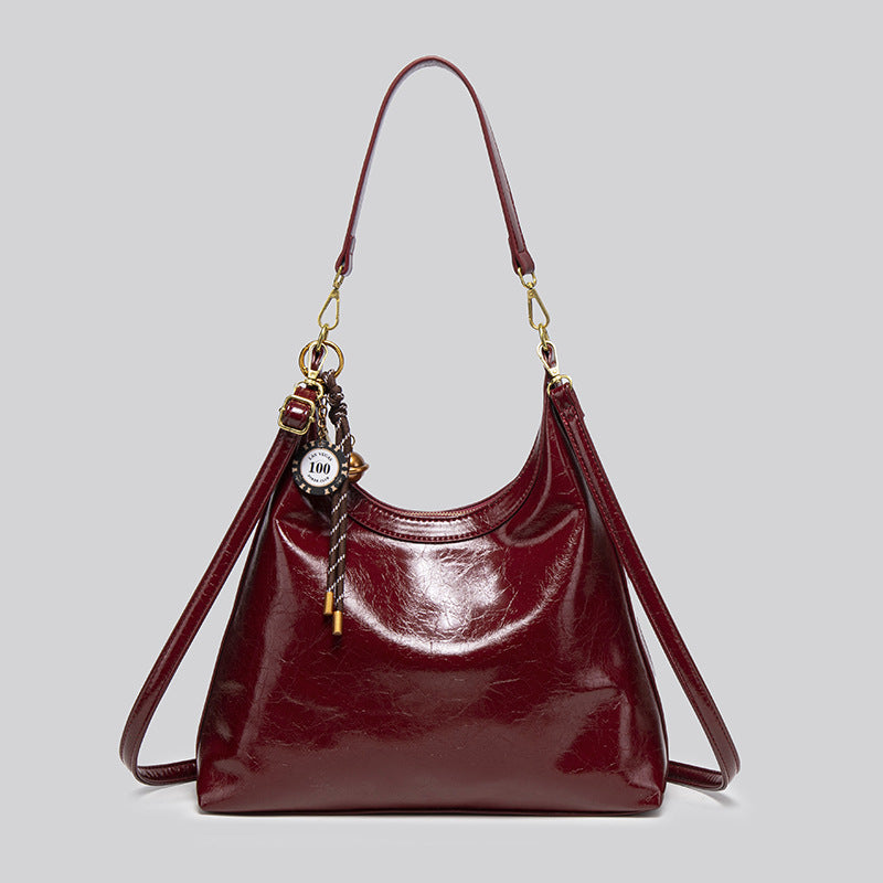 Große glänzende Hobo-Schultertasche in tiefem Burgunderrot mit Obermaterial in Lederoptik, Details in Goldoptik und dekorativem geflochtenem Anhänger, Vorderansicht