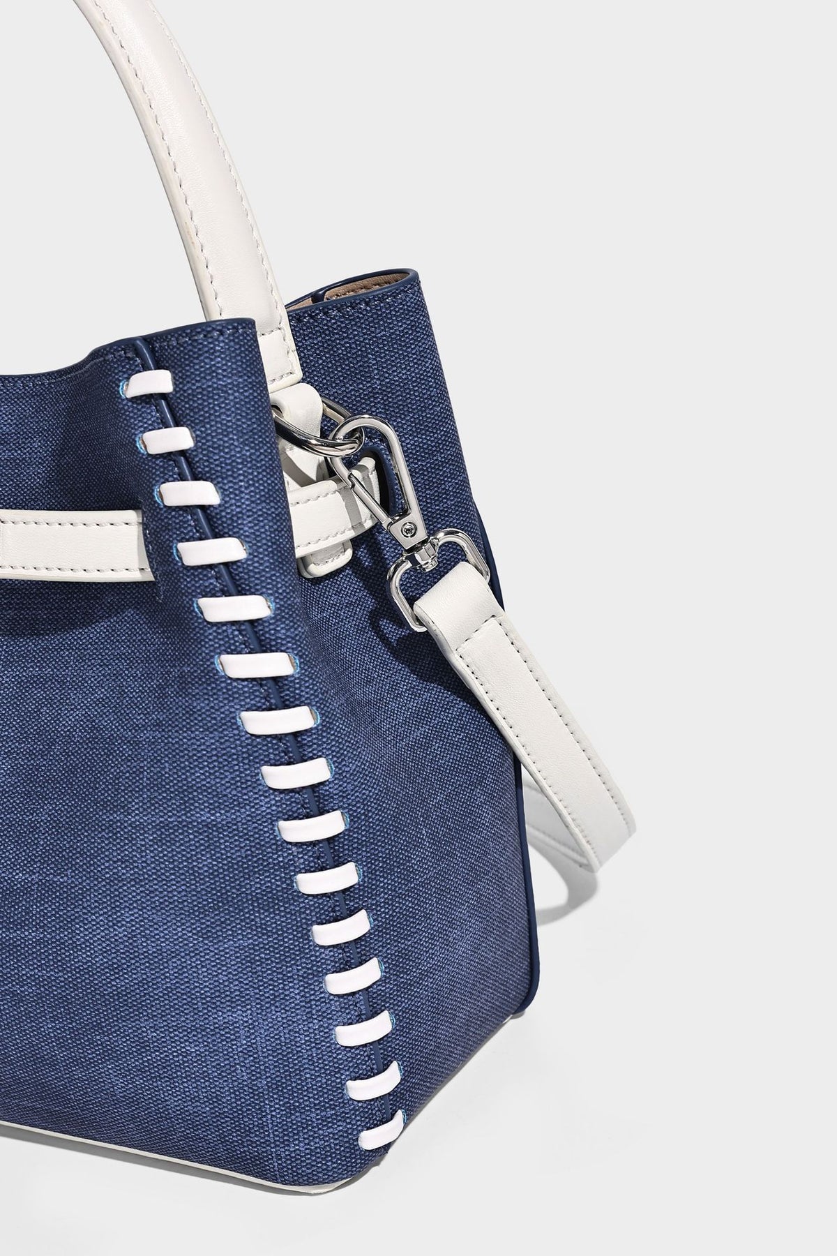 Formstabile Beuteltasche aus Denim mit weißem Zierstich-Besatz, silberfarbenem Drehverschluss, kurzen Henkeln und einem langen verstellbaren