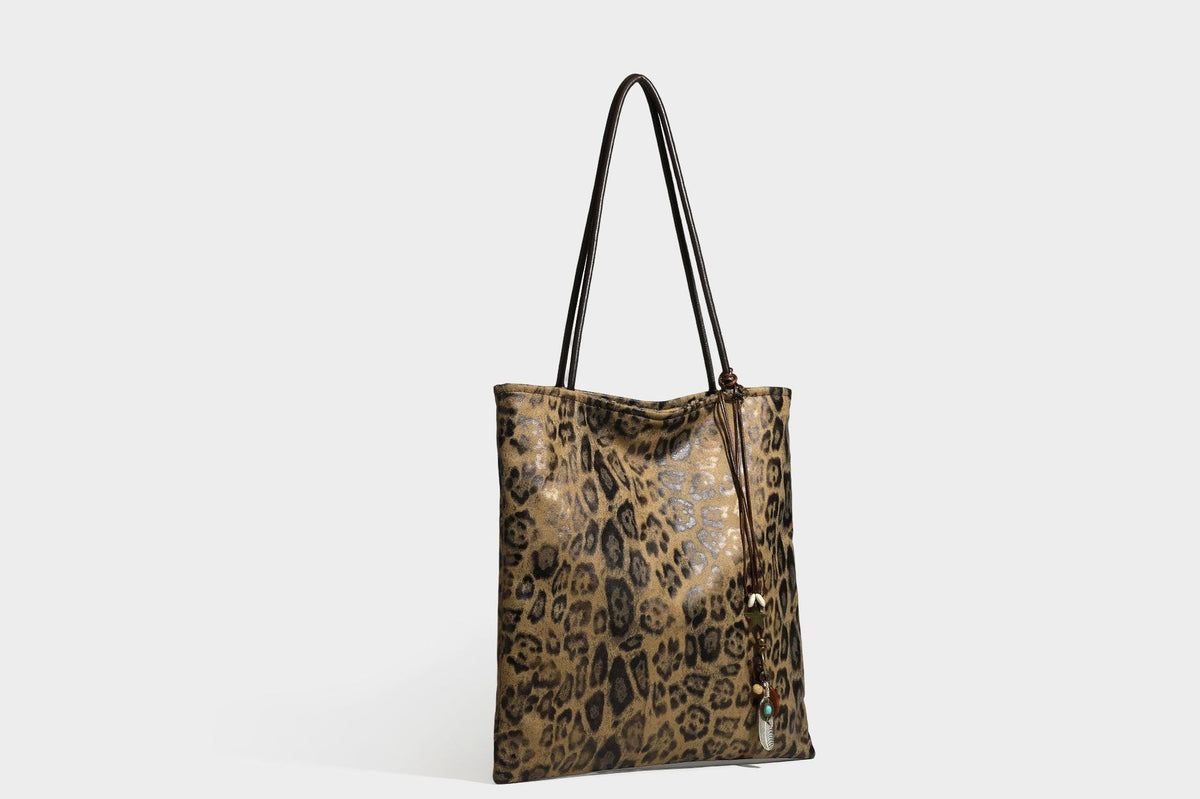 Large leopard print shoulder tote bag in tan and brown with slim dark straps and dangling beaded charm hardware, detail view