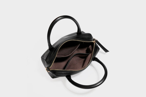 Small structured pillow satchel bag with pebbled leather-look finish, dual rolled top handles, gold-tone gourd emblem, and