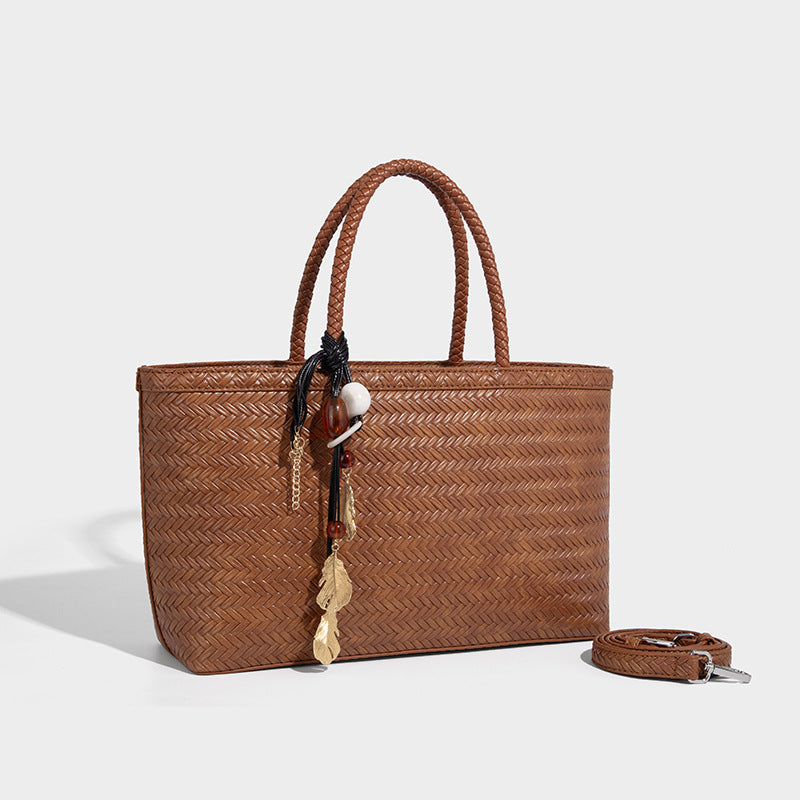 Structured woven-texture tote bag with brown braided top handles, decorative tassel charm, and detachable shoulder strap