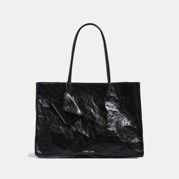 Structured rectangular crinkle leather-look tote bag with long rounded handles, zip top, and envelope-style hanging tag