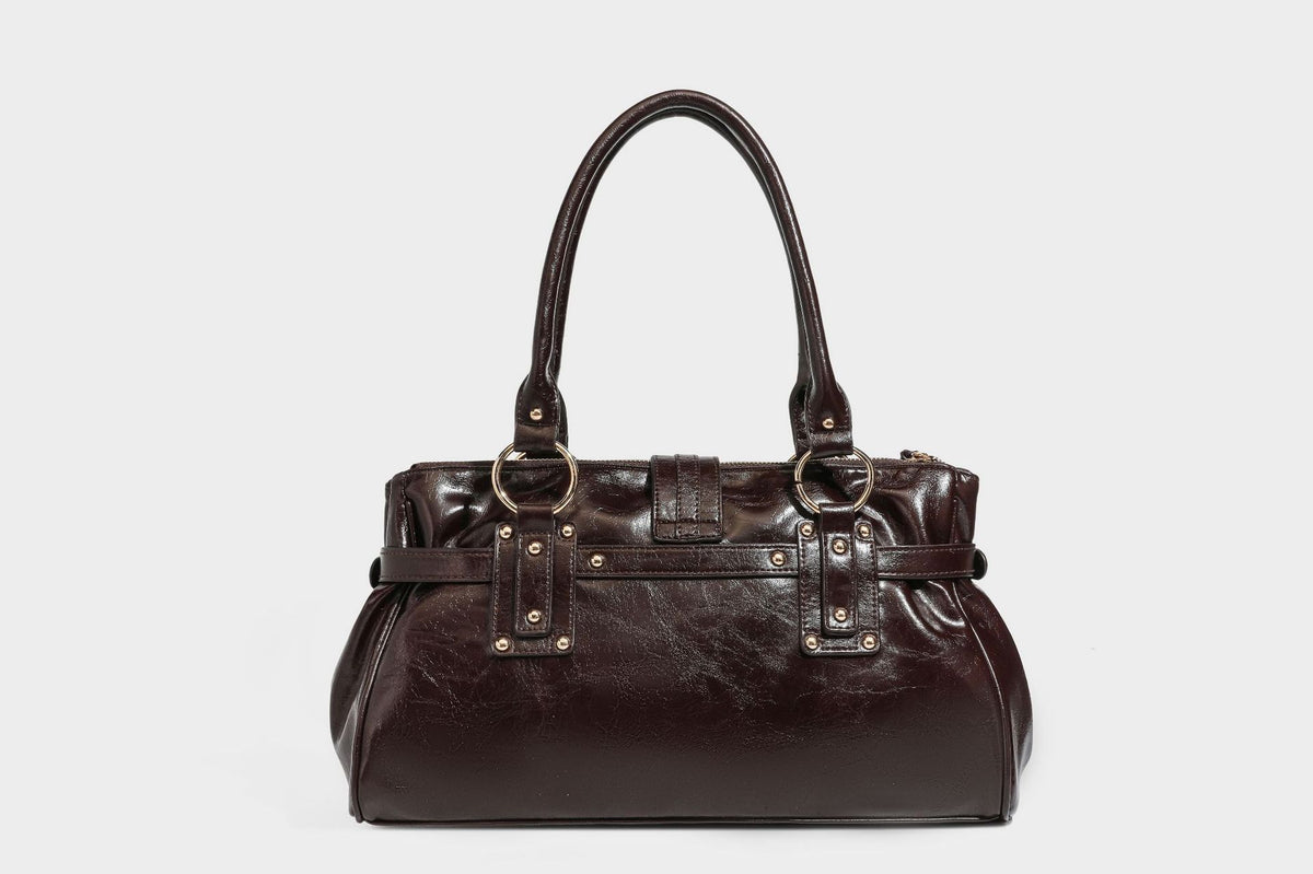 Glänzende Henkeltasche in Lederoptik mit zwei Tragegriffen, goldfarbenen Nieten und Ringen, dekorativem Schnallriemen auf der Vorderseite und