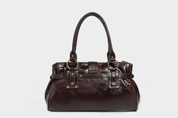Glänzende Henkeltasche in Lederoptik mit zwei Tragegriffen, goldfarbenen Nieten und Ringen, dekorativem Schnallriemen auf der Vorderseite und