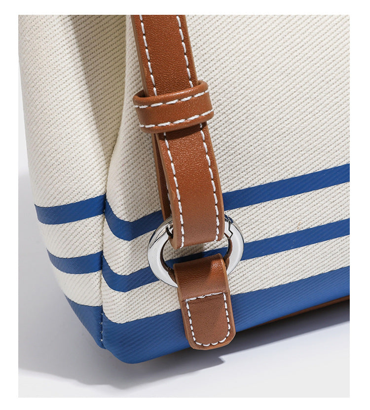 Cream canvas bucket bag with blue horizontal stripes, tan leather-look flap and trim, drawstring closure, silver-tone, detail