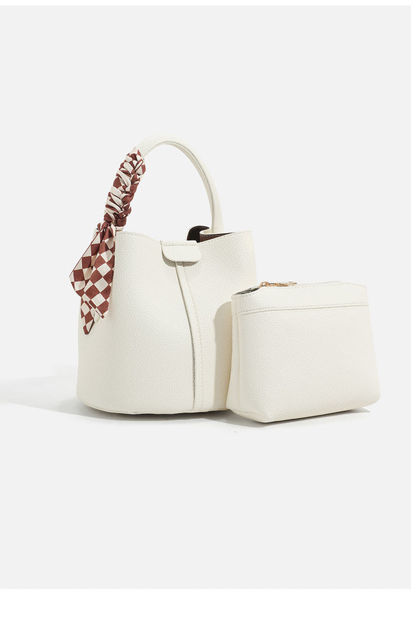 Pebbled leather-look bucket bag with checkered scarf-wrapped top handle, flap tab closure, gold-tone hardware, and matching