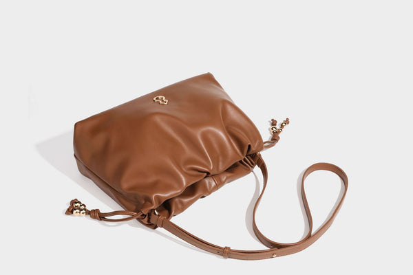 Slouchy ruched drawstring shoulder bag in smooth leather-look finish with gold-tone emblem and slim adjustable strap, detail