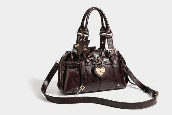 Structured leather-look satchel bag with heart padlock charm, star charm, gold-tone buckle hardware, dual top handles, and